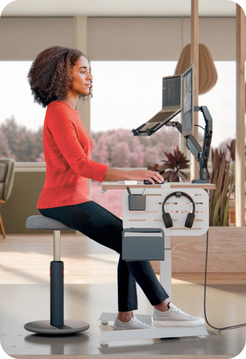 Woman working at an ergonomic sit-stand desk in a modern office promoting comfort and wellbeing